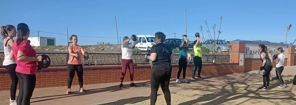 Alumnas trabajando brazos con discos de pesas en un paseo al aire libre, en un día soleado