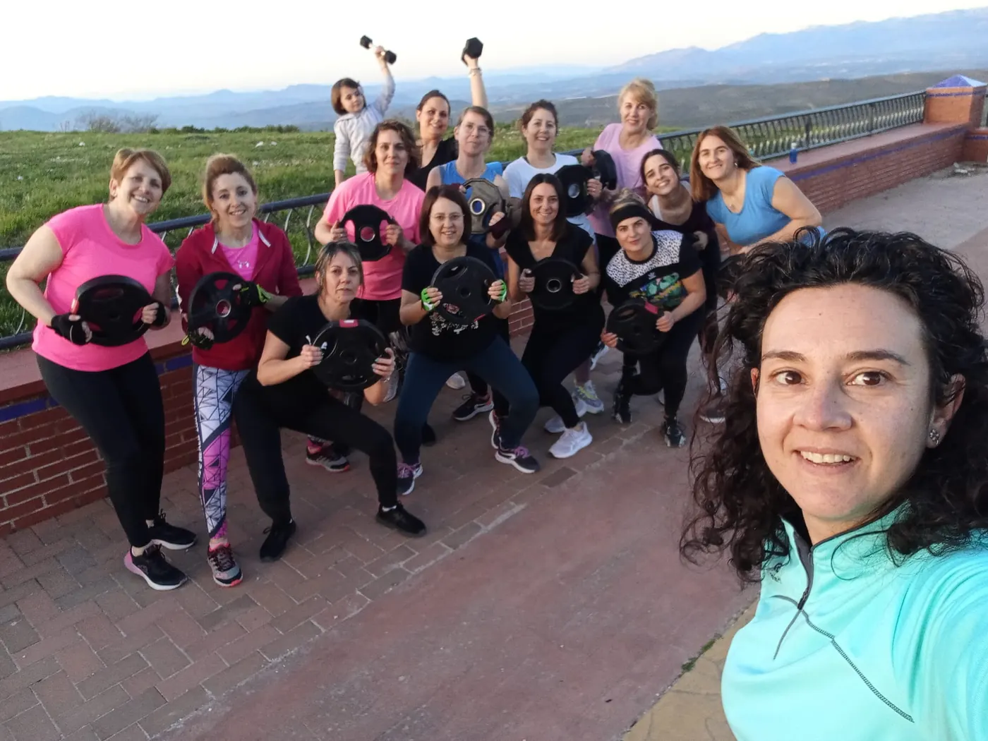 Selfie de la monitora con un grupo de alumnas haciendo sentadillas con discos al aire libre, al atardecer y con las montañas de fondo
