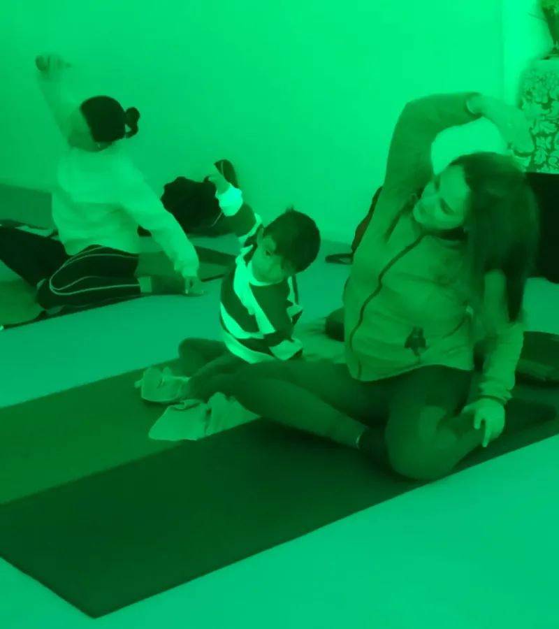 Pilates en familia: una madre y su hijo pequeño hacen un estiramiento lateral sobre la esterilla, con luz verde